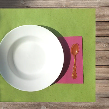 Apparecchiatura su carta paglia verde, tovagliolo di carta fucsia, piatto bianco e cucchiaino di plastica arancione